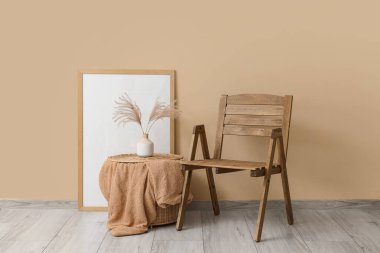 Çerçevesi, battaniyesi ve vazosu bej duvarın yanında olan rahat ahşap sandalye.