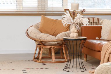 Oturma odasının içinde deri kanepe, hasır koltuk ve pencerenin yanındaki kahve masası.