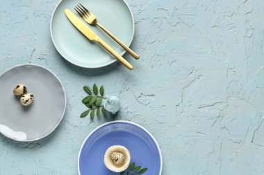 Farklı temiz tabaklar, bıldırcın yumurtaları, oyuncak tavşan ve mavi arka planda taze yeşil yapraklar. Paskalya kutlaması