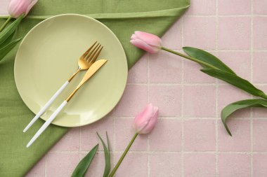 Çatal bıçak takımı, peçete ve pembe fayanslı laleler.