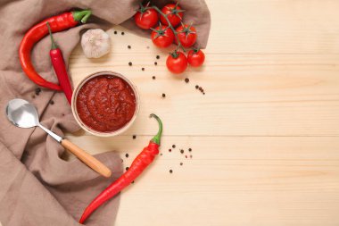 Bir kase kırmızı biber sosu ve ahşap arka planda farklı malzemeler.
