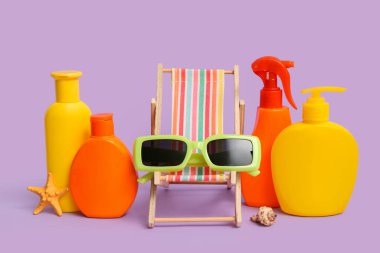 Güneş gözlüğü, dekoratif iskemle ve leylak arkaplanda güneş kremi şişeleri.