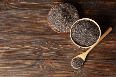 Ahşap zemin üzerinde chia tohumları olan kaseler ve kaşıklar.
