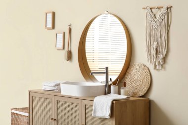 Banyodaki bej duvarın yanında lavabo, havlu ve banyo malzemeleri olan çekmeceler.