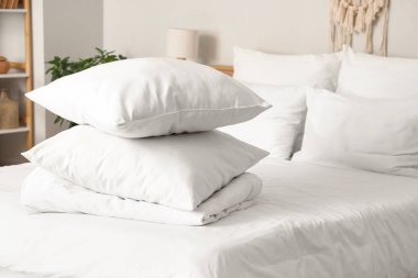 Beyaz battaniyeli rahat yatak ve şık yatak odasında yumuşak yastıklar, yakın çekim.