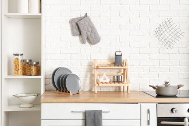 Gümüş buzdolabı ve beyaz tuğla duvarın yanındaki raf üniteli aydınlık mutfağın içi. Yakın plan.