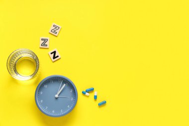 Bir bardak su, alarm saati ve sarı arkaplanda ZZZ yazan melatonin hapları.