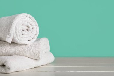 Turkuaz duvarın yanındaki beyaz masada temiz yumuşak havlular, yakın plan.