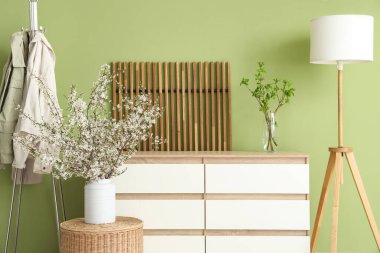 Oturma odasının içinde lamba, giysi askılığı, tuvalet ve hasır masanın üzerinde vazodaki güzel çiçek açan dallar.