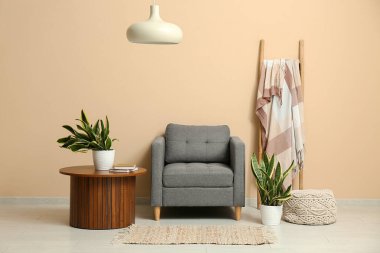 Bej duvarın yanında koltuk, masa, merdiven ve sansevieria bitkileriyle dolu bir oda.