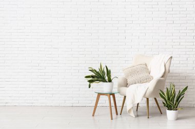 Beyaz tuğla duvarın yanında koltuk, masa ve sansevieria bitkileri olan bir oda.