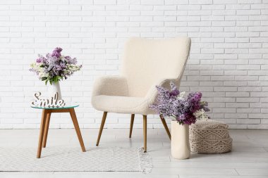 Oturma odasının içinde vazolarda koltuk, masa ve leylak çiçekleri var.