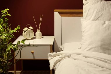 Karanlık yatak odasındaki komodinin üzerinde sazlık difüzörlü çalar saat