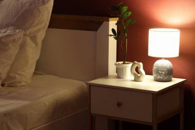 Karanlık yatak odasındaki komodinin üzerinde parlayan lamba.