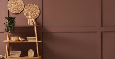 Kahverengi duvarın yanında ağaç ve dekor olan ahşap bir kitaplık. Tasarım için pankart