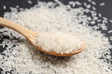 Tahta kaşık, siyah arka planda dağınık çiğ pirinç.