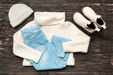 Şık çocuk süveteri, kot pantolon, şapka ve botları ahşap arka planda.