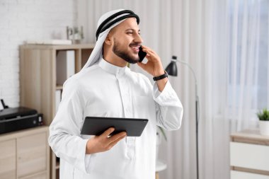 Tablet bilgisayarlı Arap işadamı ofiste cep telefonuyla konuşuyor