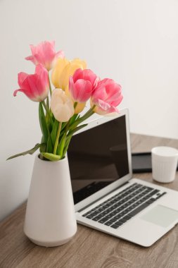 Modern dizüstü bilgisayarı ve beyaz duvarın yanında güzel çiçekleri olan şık bir çalışma alanı.