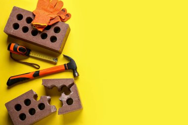 Sarı arka planda tuğlalar, eldivenler ve inşaat araçları
