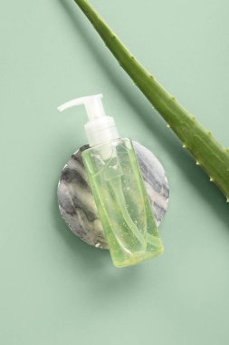 Yeşil zemin üzerinde aloe vera yaprağı olan bir şişe kozmetik ürünü.