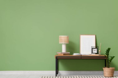 Oturma odasının içinde yeşil duvarın yanında bank, lamba ve fotoğraf çerçevesi var.