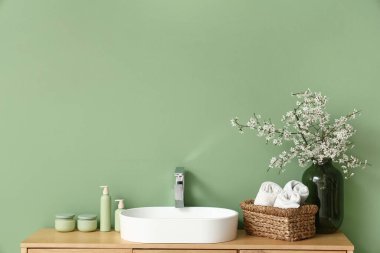 Banyodaki yeşil duvarın yanındaki çekmecelerde çiçek açan dallar ve banyo malzemeleri olan vazo.