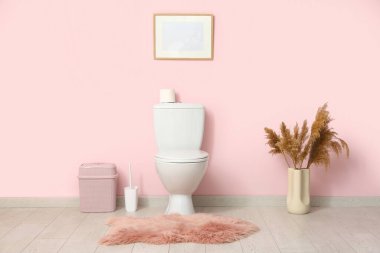 Seramik klozet, çöp kutusu ve kürk halısı olan şık bir tuvalet.