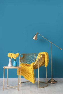 Modern koltuğu ve mavi duvarın yanındaki sehpanın üzerinde güzel narsisus çiçekleri olan şık bir oda.