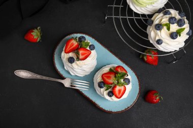 Tatlı Pavlova kekleri taze böğürtlenli ve siyah arkaplanlı nane şekerli.