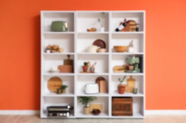 Mutfak gereçleri ve turuncu duvarın yanında bitkiler olan raf ünitesi.