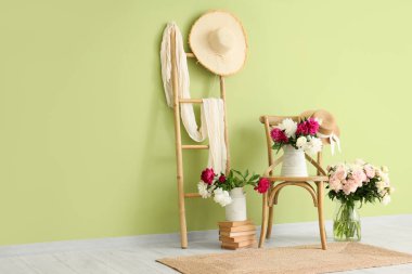 Yeşil duvarın yanında güzel şakayıklar olan sandalye ve vazolar.