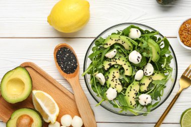 Sağlıklı roka salatası ve beyaz ahşap arka planda malzemelerle dolu bir kase.