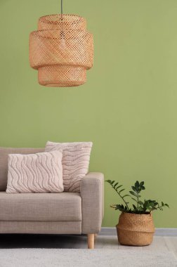 Yeşil duvarın yanında rahat gri koltuklu, çiçekli ve hasır lambalı şık bir oturma odası.