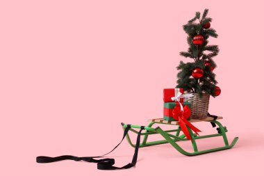 Hediye kutularıyla kızak ve pembe arka planda saksıda Noel ağacı.