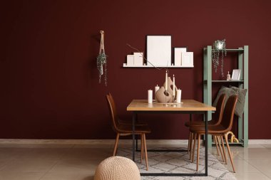 Yemek odasının içinde raflar, sandalyeler, şezlonglar ve mum tutacakları bordo duvarın yanında.