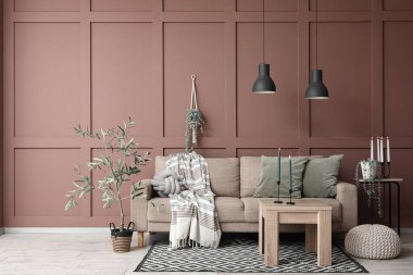 Oturma odasının içinde kanepe, ev bitkileri, komodin ve mum tutacakları kahverengi duvarın yanındaki sehpanın üzerinde.