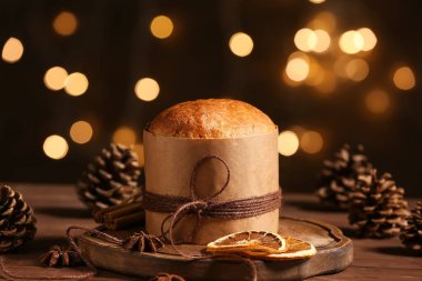 Orman çıkıntıları, baharatlar ve kurumuş portakallarla kahverengi ahşap masada bulanık çelenk arka planına karşı lezzetli Noel Panettone.