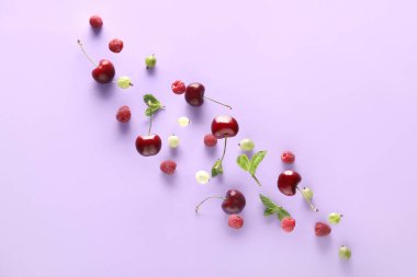 Farklı meyveler ve yeşil yapraklar leylak arka planda uçuşuyor.