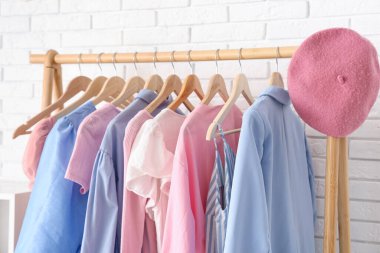 Beyaz tuğla duvarın yanında şık giysileri ve şapkası olan ahşap askı, yakın plan.