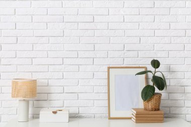 Odadaki beyaz tuğla duvarın yanındaki çekmecelerin üzerindeki lamba ve saksı, yakın plan.