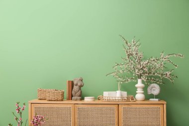 Oturma odasındaki yeşil duvarın yanında vazo dolusu beyaz dallar ve dekor olan bir elbise.