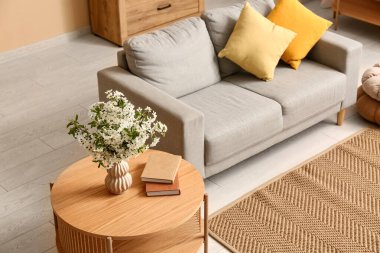 Oturma odasındaki kanepenin yanındaki sehpanın üzerine kitap konmuş beyaz çiçek açan bir vazo.