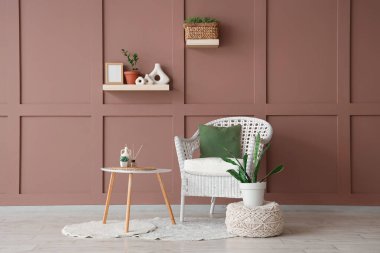 Masa, puf ve hasır koltuk, odanın içindeki kahverengi duvarın yanında.