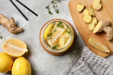 Gri arkaplanda kekik, zencefil ve limon dilimleri olan bir bardak erimiş su.