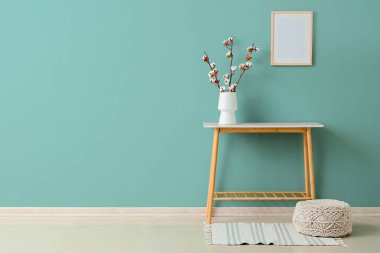 Oturma odasının içindeki yeşil duvarın yanında pamuk çiçekli vazo, masa ve vazo.