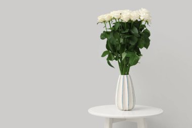 Masanın üzerinde, arka planda duran vazoda duran güzel beyaz güller.