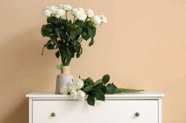 Bir buket güzel beyaz gül vazonun içinde, çekmecelerin üstünde bej arka planda.