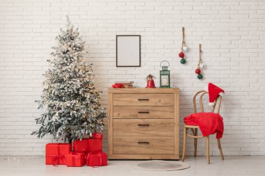 İçinde Noel ağacı, sandalye, hediye kutuları, beyaz tuğla duvarın yanındaki klozette farklı süslemeler ve fener olan bir oda.