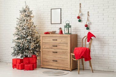 İçinde Noel ağacı, sandalye, hediye kutuları, beyaz tuğla duvarın yanındaki klozette farklı süslemeler ve fener olan bir oda.